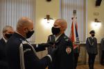 w sali Komendant Policji przypina medal do klapy munduru funkcjonariusza Służby Celno-Skarbowej,  w tle, przy ścianie stoi poczet sztandarowy Policji, wszystkie osoby mają maseczki na twarzach
