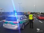 funkcjonariusz KAS stoi przy radiowozie  zatrzymując ruch samochodów na autostradzie A4